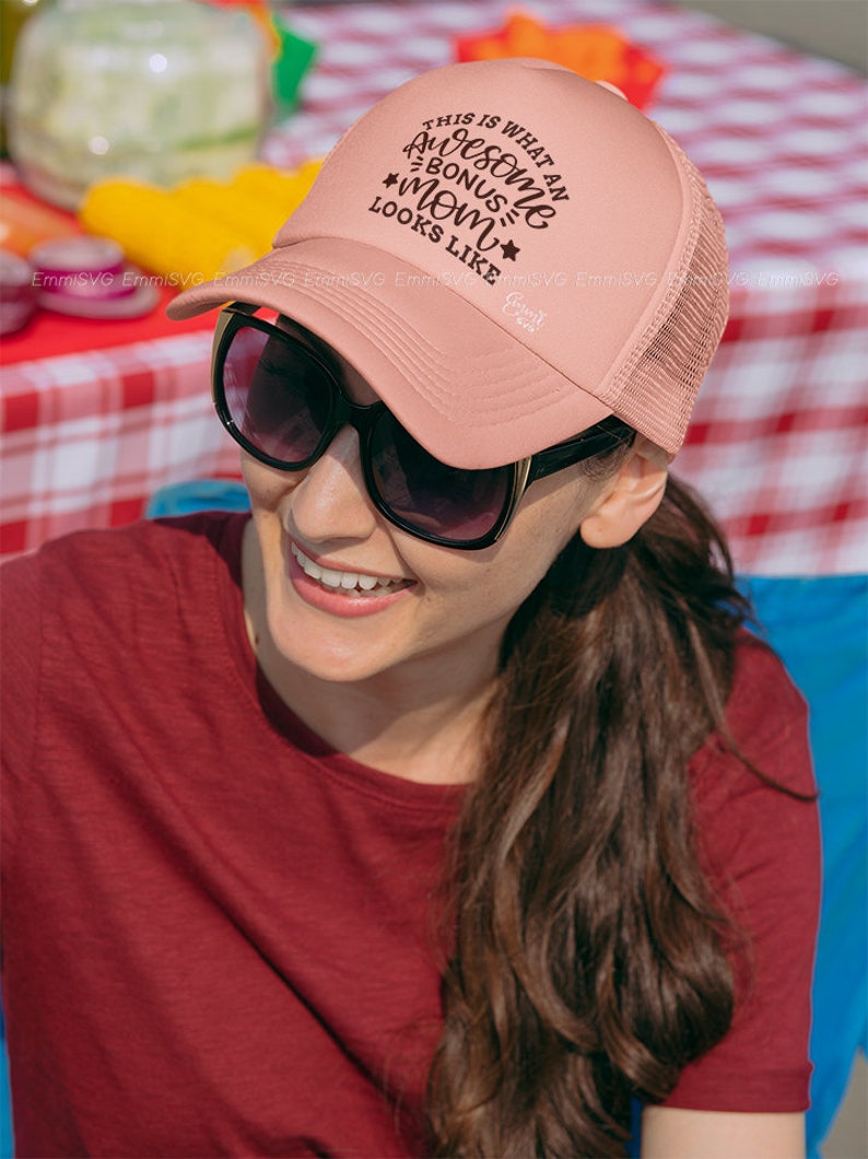 May include: A pink trucker hat with a brown embroidered design that says "This is what an awesome bonus mom looks like".
