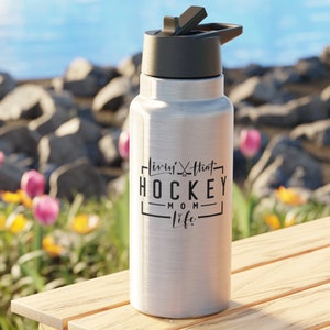 May include: Silver water bottle with a black lid and a black graphic that says "Livin' that Hockey Mom Life" on it.