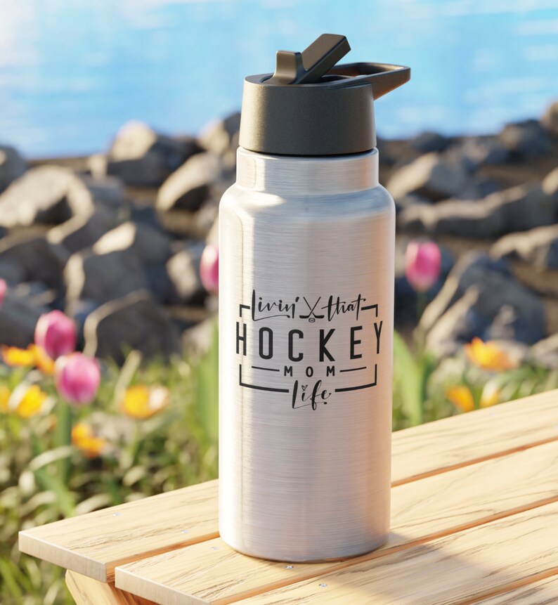 May include: Silver water bottle with a black lid and a black graphic that says "Livin' that Hockey Mom Life" on it.