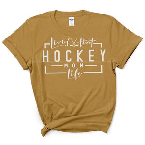 May include: A mustard yellow t-shirt with white text that reads "Livin' that Hockey Mom Life".