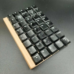 May include: A black keyboard with white lettering. The keys are arranged in a standard layout with function keys (F1-F12), arrow keys, and other common keys. The keyboard is made of plastic and has a brown cardboard backing.
