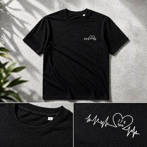 Può includere: T-shirt nero con un disegno a battito cardiaco bianco e un cuore con "174 bpm" stampato sul petto. La maglietta ha maniche corte e girocollo. Il design è minimalista.