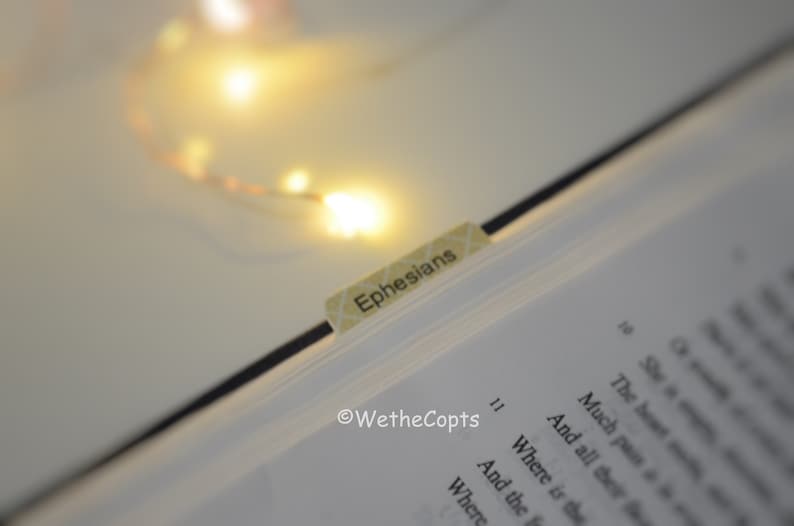 May include: A close-up of a book with a bookmark that says "Ephesians". The book is open to a page with the text "Where is the" and "And the". The text "WetheCopts" is visible at the bottom of the page.