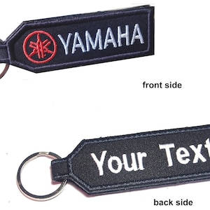 Puede incluir: Llavero negro con un logotipo de Yamaha rojo y blanco en la parte delantera y el texto "Your Text" en la parte posterior.