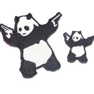 Puede incluir: Dos parches bordados de panda blanco y negro sosteniendo pistolas. El panda más grande está de pie con la pata izquierda levantada y el panda más pequeño está de pie con las dos patas juntas. Ambos pandas están mirando hacia adelante.