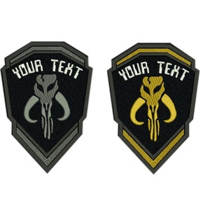 May include: Four embroidered patches featuring a Mandalorian symbol and the text "YOUR TEXT" in white. The patches are in red, grey, gold, and green.