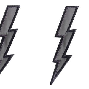 Könnte beinhalten: Zwei silberne Blitz-Patches mit schwarzen Nähten.