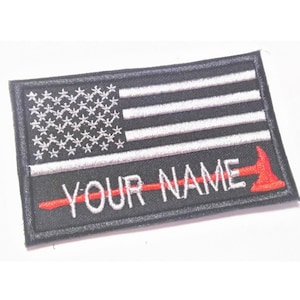 Könnte beinhalten: Schwarz-weißes amerikanisches Flaggen-Patch mit einer roten Linie und einer Axt. Der Text "YOUR NAME" ist in Weiß unter der Flagge gestickt.