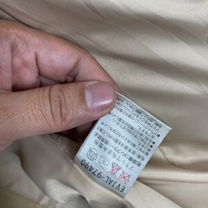 May include: A beige fabric label with black text and a red and white symbol. The text reads "EVJAL-97490" and includes instructions for caring for the fabric. The symbol is a red "X" over a red circle.