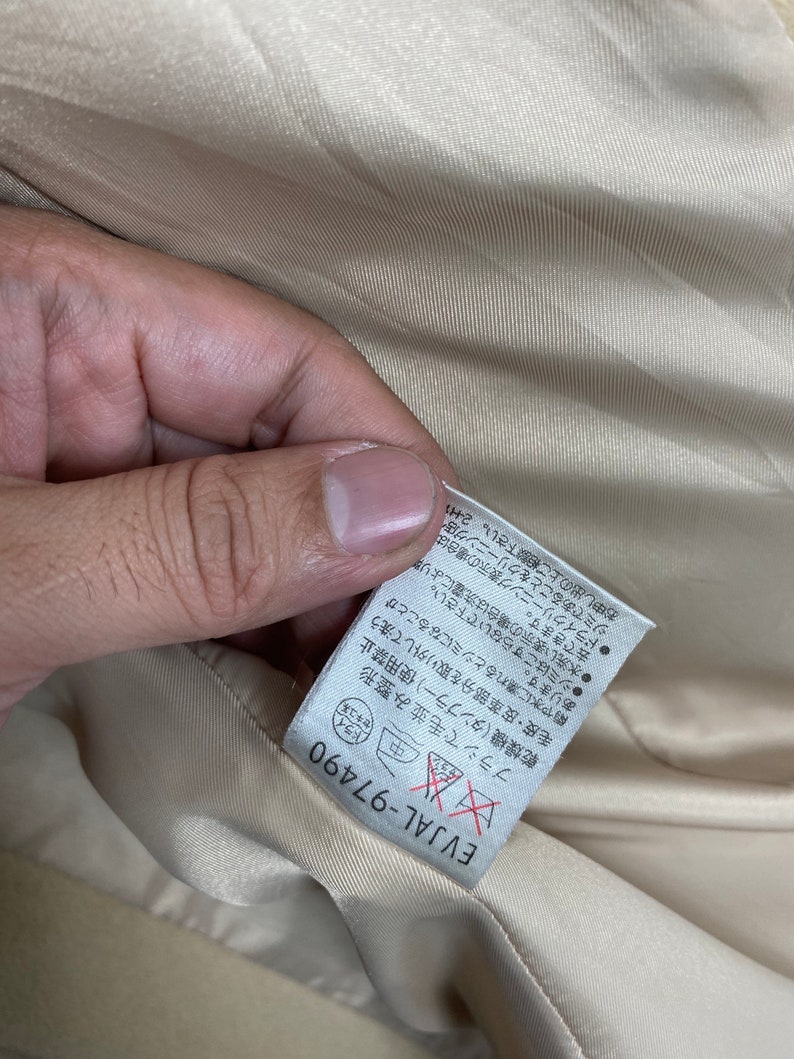 May include: A beige fabric label with black text and a red and white symbol. The text reads "EVJAL-97490" and includes instructions for caring for the fabric. The symbol is a red "X" over a red circle.
