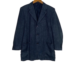 May include: A dark blue blazer with a single-breasted button closure and two flap pockets. The blazer has a subtle herringbone pattern and is hanging on a wooden hanger.