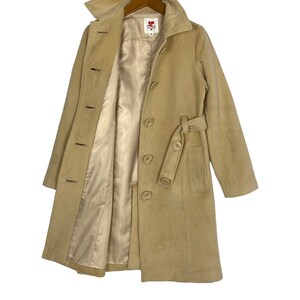 May include: A beige wool coat with a belt and a button closure. The coat has a satin lining and a red label with the text "RC" on it.