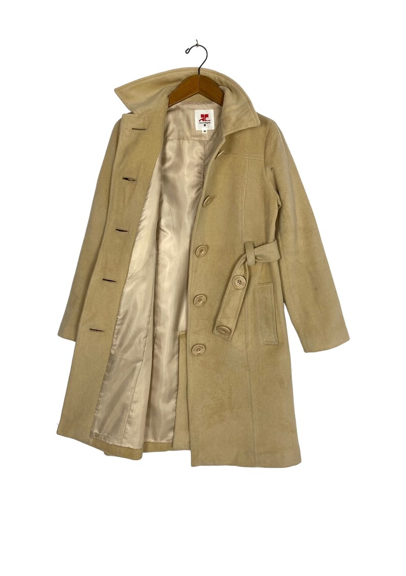 May include: A beige wool coat with a belt and a button closure. The coat has a satin lining and a red label with the text "RC" on it.