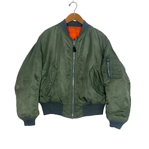 May include: A green bomber jacket with a zip fastening and a zipped pocket on the left sleeve. The jacket has a ribbed knit collar, cuffs, and waistband.