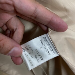 May include: A white tag with black text that reads "SCG MADE IN CHINA" and lists the fabric composition as 63% angora and 37% wool. The tag also states that the fur trim is fox and the lining is polyester.
