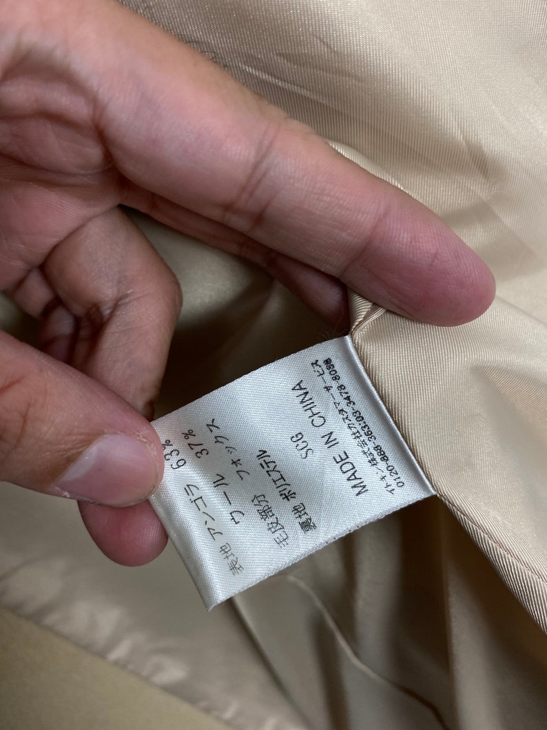 May include: A white tag with black text that reads "SCG MADE IN CHINA" and lists the fabric composition as 63% angora and 37% wool. The tag also states that the fur trim is fox and the lining is polyester.