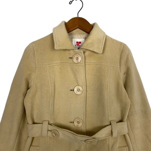 May include: A beige wool coat with a belt and five large buttons. The coat has a collar and long sleeves. The label on the coat reads "JC Collection".