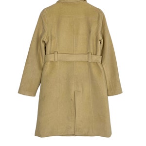 May include: A beige wool coat with a belt and a collar. The coat is hanging on a wooden hanger.