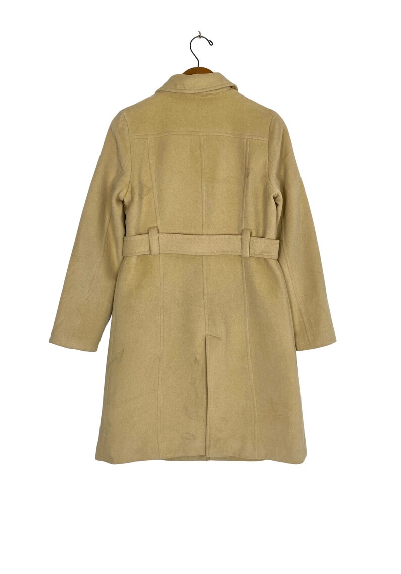 May include: A beige wool coat with a belt and a collar. The coat is hanging on a wooden hanger.