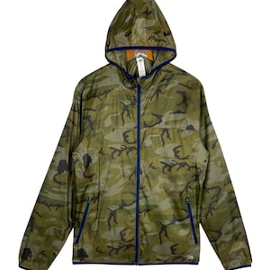 Peut inclure: Un coupe-vent léger à capuche avec un motif camouflage vert, marron et noir. La veste présente une fermeture éclair frontale bleu foncé, des bordures bleu foncé assorties sur la capuche et les poignets, ainsi que deux poches latérales zippées.