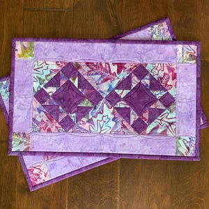 Puede incluir: Dos caminos de mesa acolchados de color morado y blanco con un patrón de hojas y un diseño geométrico en el centro.