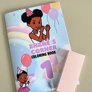 Pode incluir: Um livro de colorir intitulado Zhane's Corner Coloring Book 1 com uma ilustração de desenho animado de duas crianças com chapéus de festa, balões e um arco-íris, acompanhado por um objeto retangular rosa claro liso.