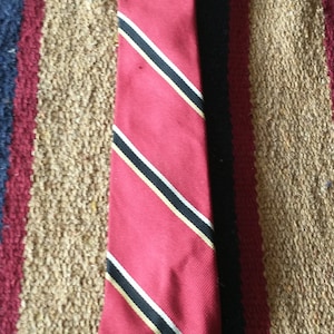 May include: A red tie with black and white stripes and a gold accent. The tie is made of a silky material.