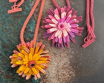 May include: Two beaded necklaces with flower pendants. The necklaces are made of small, coral-colored beads. The pendants are made of pink, orange, and yellow beads. The pendants are shaped like flowers with multiple layers of petals.