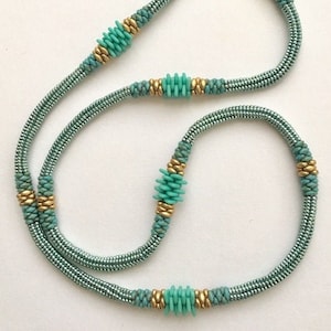 Könnte beinhalten: Eine lange türkisfarbene und goldene Perlenkette mit mehreren Strängen und dekorativen Perlen.