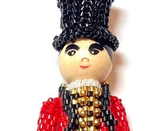 Puede incluir: Una muñeca de cuentas con un sombrero de copa negro, una chaqueta roja y un chaleco negro y dorado. La muñeca tiene una cara de madera pintada con una sonrisa.