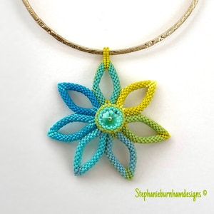 May include: A beaded flower pendant necklace with a turquoise, green, and yellow color scheme. The pendant is attached to a gold chain.