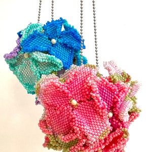 May include: Three beaded flower charms hanging from silver chains. The flowers are pink, blue, and green.