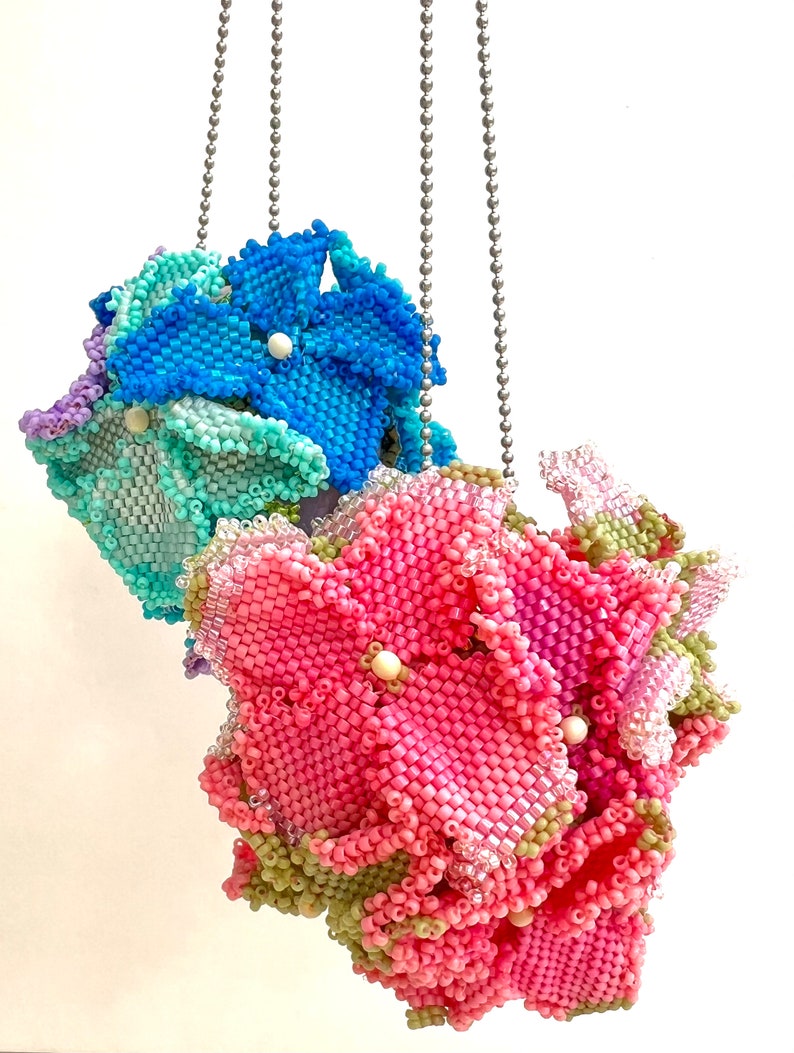 May include: Three beaded flower charms hanging from silver chains. The flowers are pink, blue, and green.