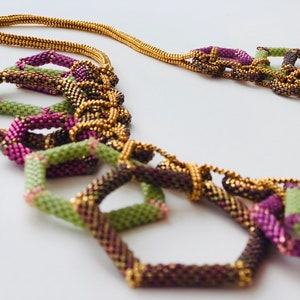 May include: A multi-colored beaded necklace with gold accents. The necklace is made of small, square beads in shades of green, purple, and brown. The beads are arranged in a geometric pattern, creating a unique and stylish look.