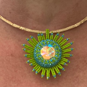 May include: A gold choker necklace with a green and blue beaded sunburst pendant. The pendant features a large iridescent crystal in the centre.