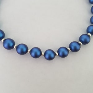 May include: A close-up of a blue beaded necklace with silver accents. The beads are round and have a matte finish.