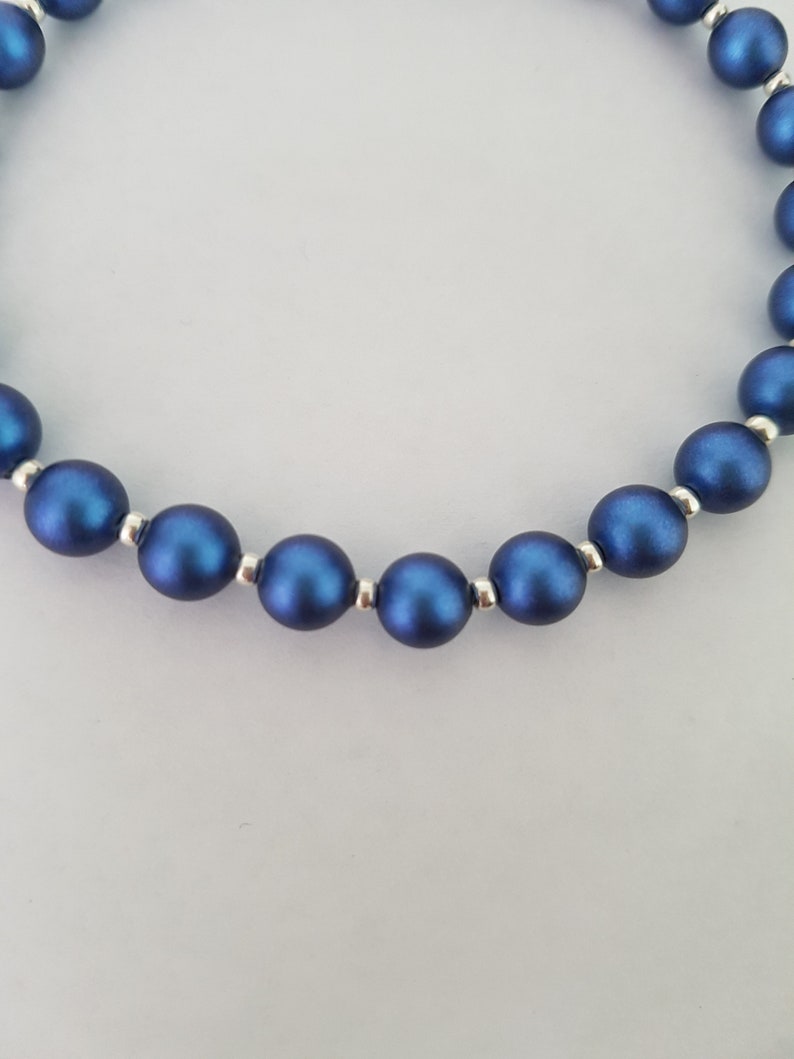 May include: A close-up of a blue beaded necklace with silver accents. The beads are round and have a matte finish.
