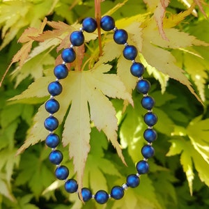 May include: A blue beaded bracelet with silver accents, photographed against a backdrop of yellow and green leaves.