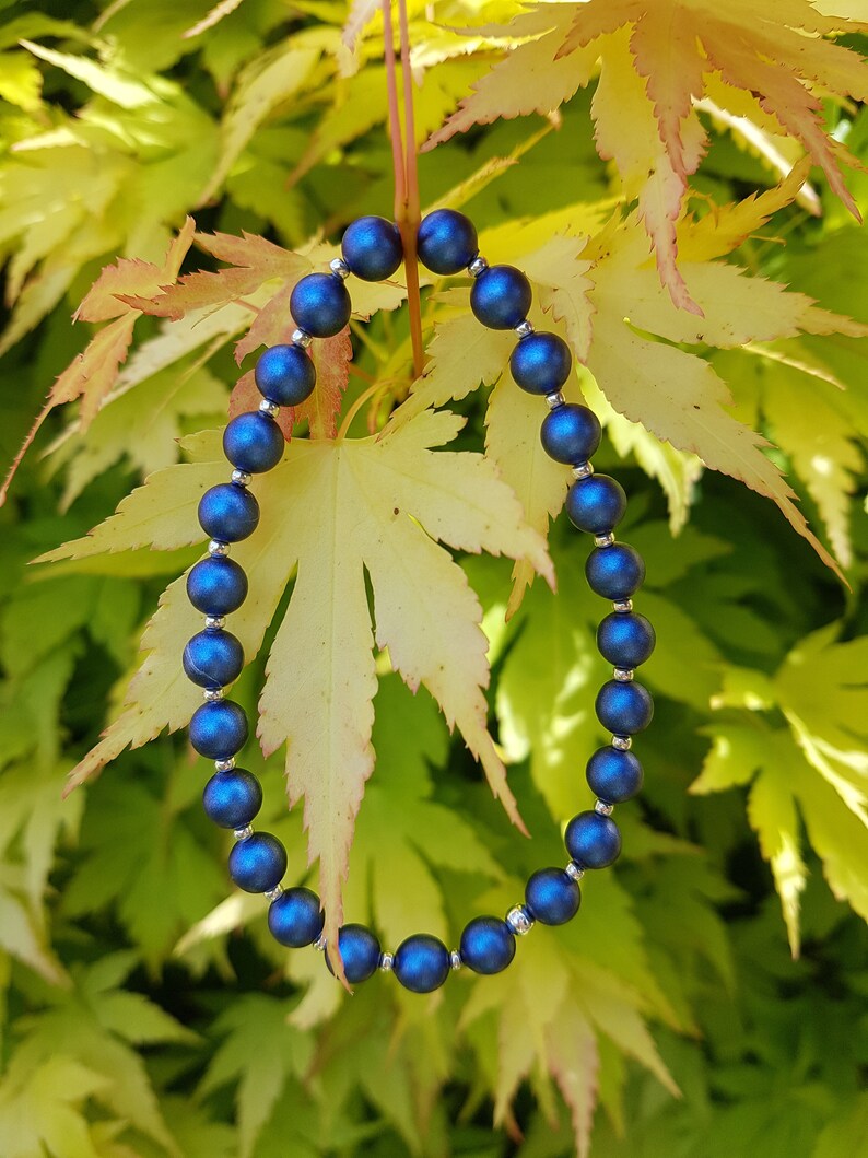 May include: A blue beaded bracelet with silver accents, photographed against a backdrop of yellow and green leaves.