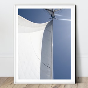 Puede incluir: Una vista cercana de una vela de velero blanca ondeando en el viento contra un cielo azul brillante. La vela está tensa y las líneas son visibles. El sol brilla intensamente, proyectando un resplandor en la vela.
