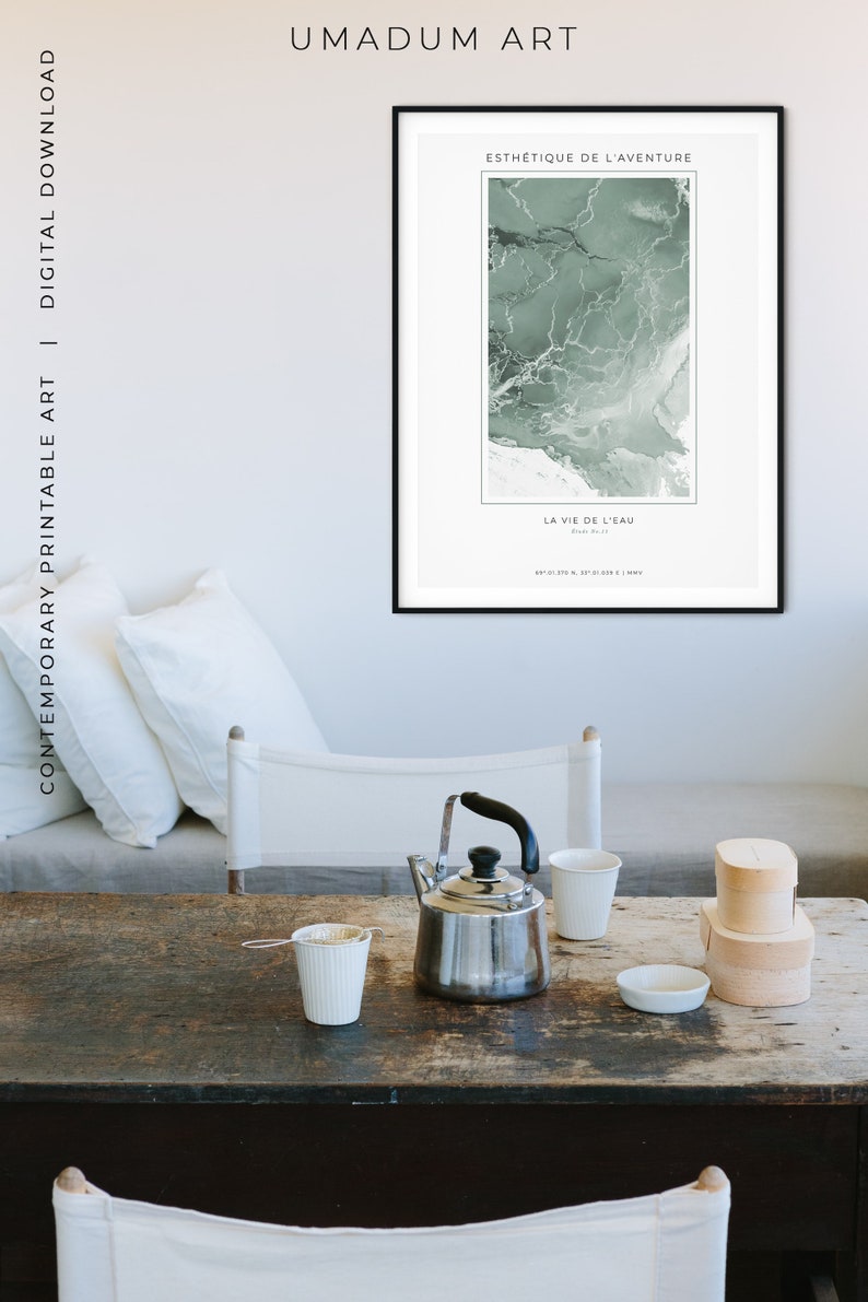 May include: A black framed print with a green abstract design and the text "ESTH&Eacute;TIQUE DE L'AVENTURE" and "LA VIE DE L'EAU". The print is hanging on a wall in a room with a wooden table, a teapot, and two cups.