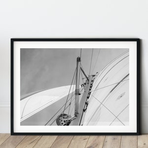 May include: Black and white photograph of a sailboat's rigging, showing the mast and sail in detail.
