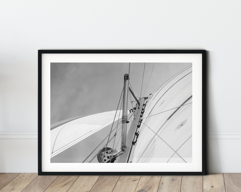 May include: Black and white photograph of a sailboat's rigging, showing the mast and sail in detail.
