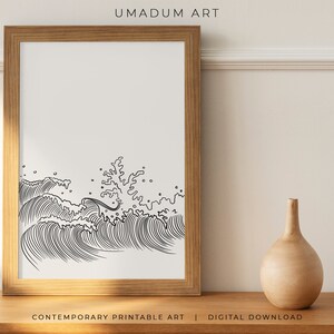 K&ouml;nnte beinhalten: Eine Schwarzwei&szlig;-Zeichnung von Ozeanwellen, die gegeneinander krachen. Das Bild ist in einem hellbraunen Holzrahmen gerahmt und auf einer Holzoberfl&auml;che ausgestellt. Der Text "UMADUM ART" befindet sich oben im Bild und der Text "CONTEMPORARY PRINTABLE ART | DIGITAL DOWNLOAD" unten im Bild.