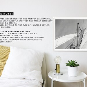 May include: Black and white photograph of a sailboat with the sail billowing in the wind. The photo is framed in a white frame and hanging on a white wall.