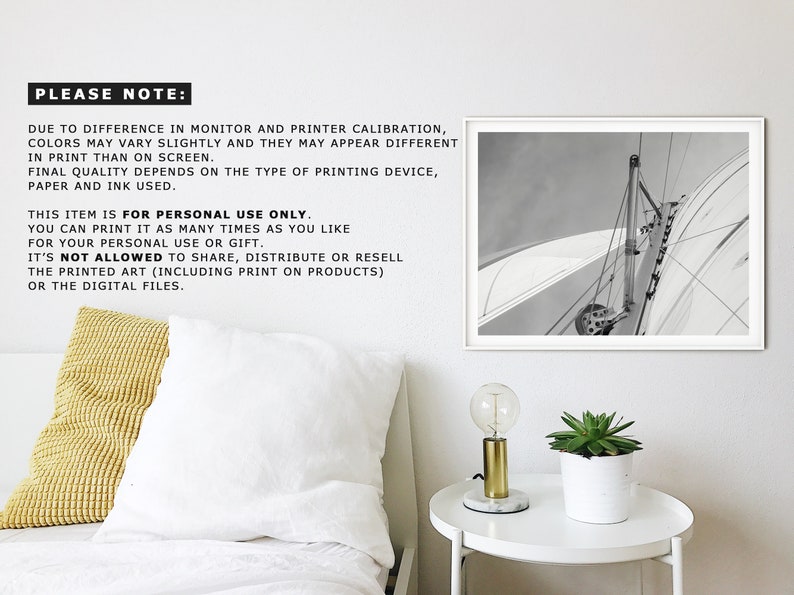 May include: Black and white photograph of a sailboat with the sail billowing in the wind. The photo is framed in a white frame and hanging on a white wall.