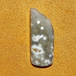 May include: A gray and white agate stone with a unique pattern of white swirls and spots. The stone is smooth and polished, and it has a natural, organic shape.