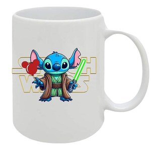 May include: White ceramic mug featuring a cartoon character resembling Stitch from Lilo & Stitch, dressed as Yoda from Star Wars. The character holds a green lightsaber and red balloons. The Star Wars logo is in gold.