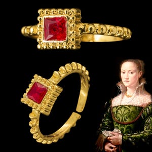 Op de afbeelding: Een gouden ring met een rode vierkante edelsteen gezet in een gedetailleerd, versierd frame. De ring is verstelbaar en heeft een eenvoudige band.