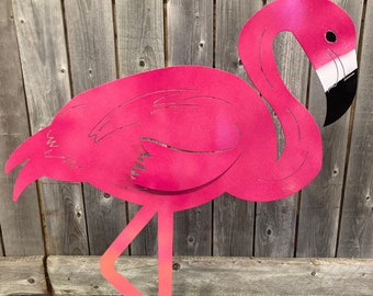 May include: A vibrant pink metal flamingo yard art. The flamingo has a long neck and legs, with a black beak and eye. The legs transition from orange to pink. The flamingo is placed in a metal container with sand.